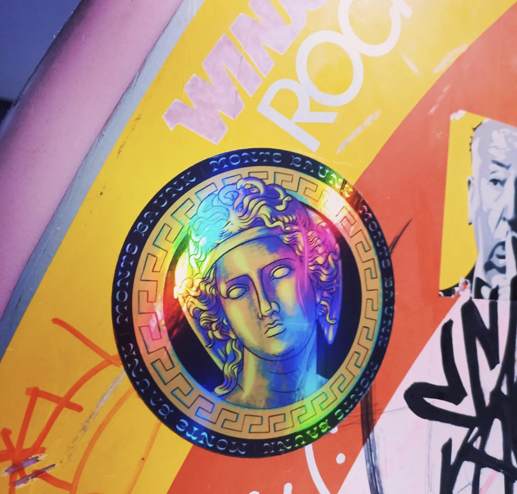 A holographic Monte Baunk sticker on a wall
